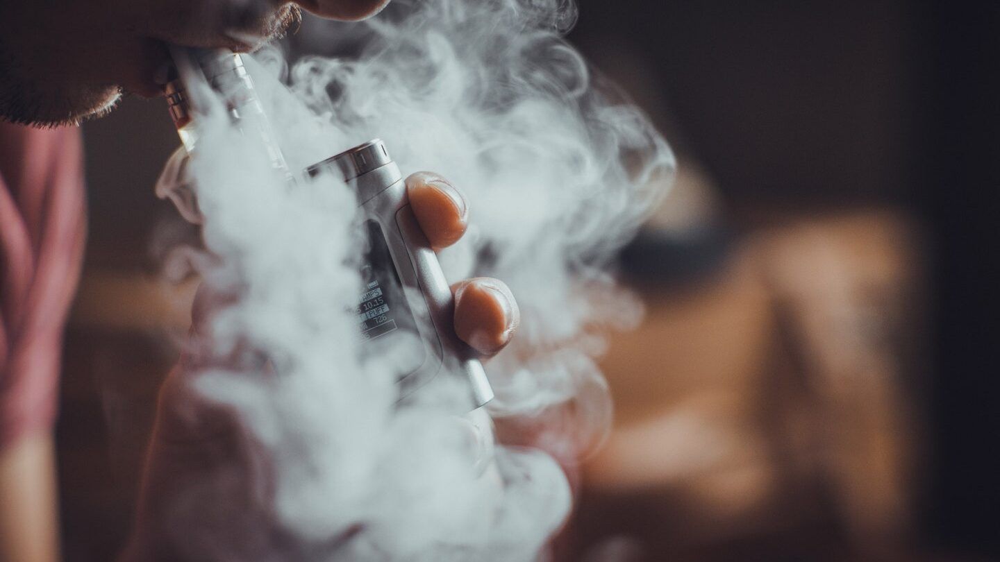 Persona inhalando de un vapeador con densa nube de vapor, es peligroso fumar un vapeo caducado descubre las consecuencias aqui