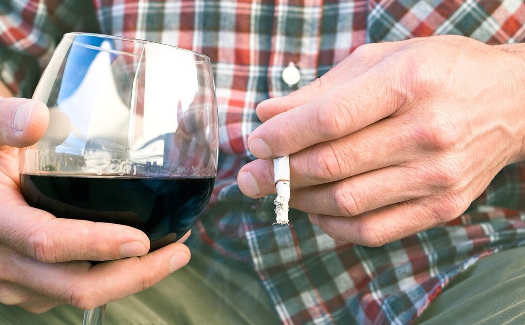 Persona sosteniendo una copa de vino y un cigarrillo en la mano, es peligroso mezclar ibuprofeno y alcohol wipes descubrelo aqui