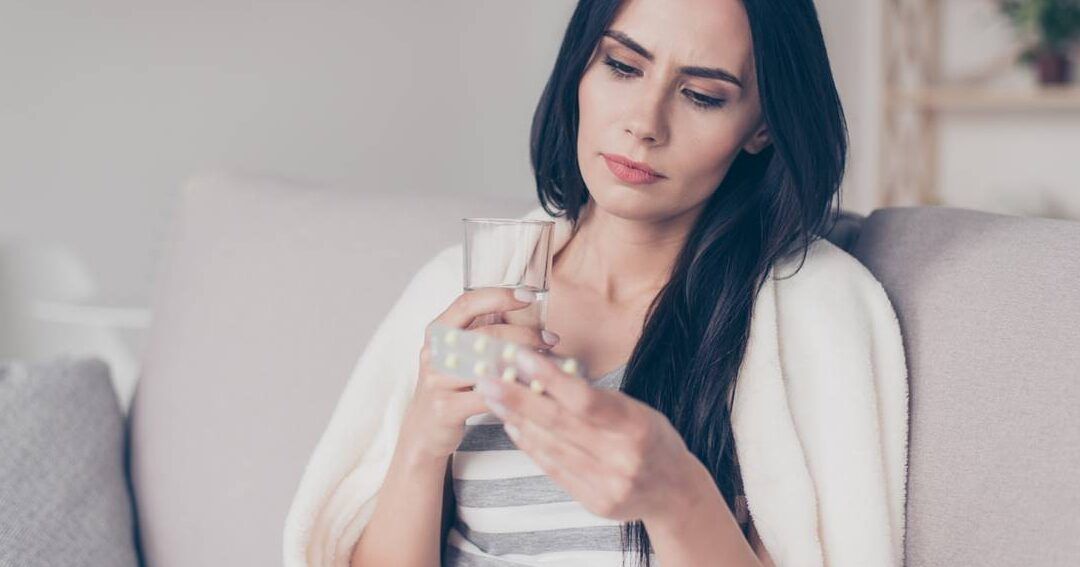 Mujer leyendo un blíster de pastillas con un vaso de agua preguntándose si es seguro mezclar ibuprofeno y paracetamol de un gramo