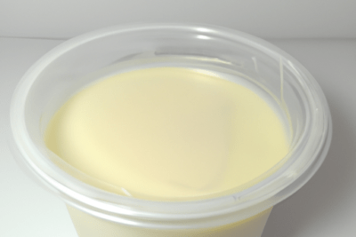 Envase de crema en vaso plástico — es seguro usar nata para cocinar caducada 3 meses | guía visual que muestra un envase plástico transparente con crema de color marfil y superficie lisa.