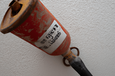 Extintor caducado por que deberias preocuparte: extintor rojo oxidado con boquilla negra montado en pared