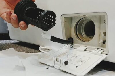 Mano sosteniendo un filtro lavadora frontal extraído junto a la tapa del compartimento