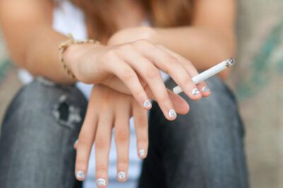 Manos con manicura sosteniendo un cigarrillo fumar con anginas que consecuencias tiene para tu salud 1