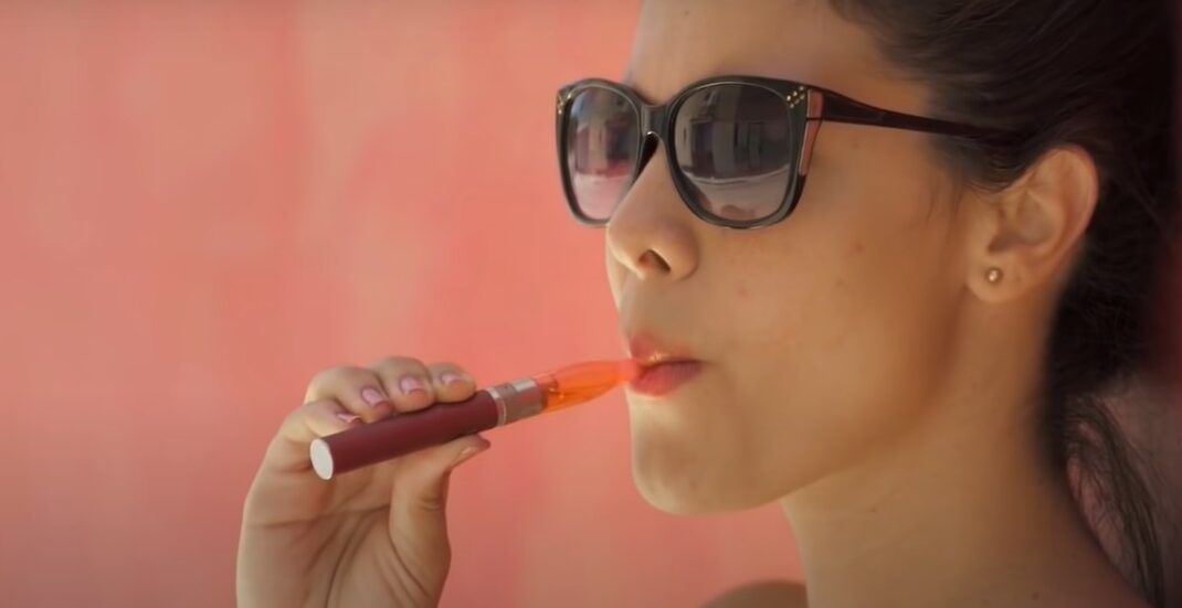 Mujer con gafas de sol inhalando de un vaporizador, fumar vaper sin liquido es peligroso descubre que sucede