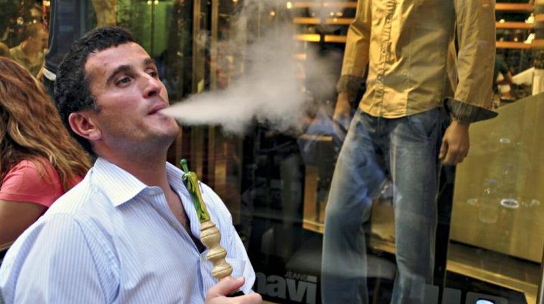 Hombre exhalando una nube de shisha frente a un escaparate, fumar vapor de agua es seguro descubre que sucede al inhalarlo