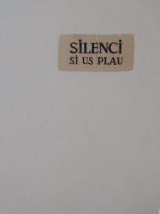 Placa cerámica con el texto 'SILENCI SI US PLAU' sobre pared blanca, hola en catalan descubre su significado palabras clave cataluna
