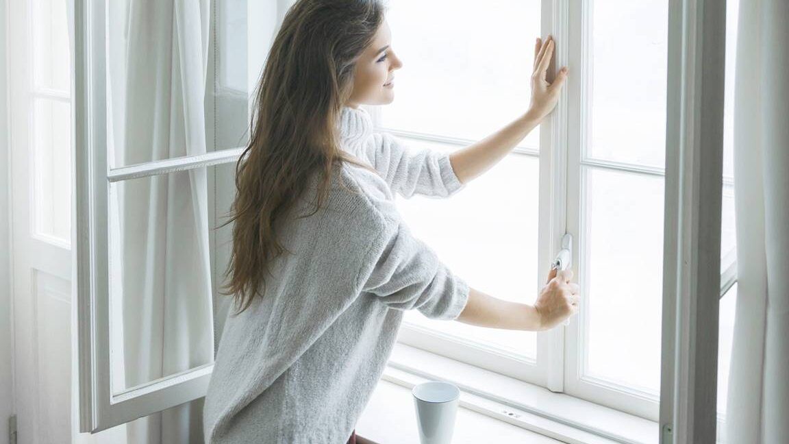 Mujer abriendo una ventana para ventilar una habitación y reducir riesgos domésticos; inhalar gas nu descubre las consecuencias de esta peligrosa practica