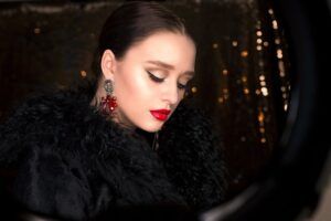 Retrato elegante de mujer con maquillaje intenso, labios rojos y abrigo negro, interpretacion simbolismo tatuaje flecha hacia abajo