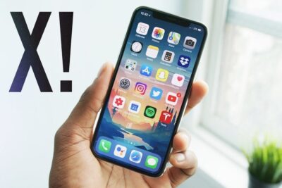 Mano sosteniendo un iphone x con la pantalla de inicio y aplicaciones visibles.
