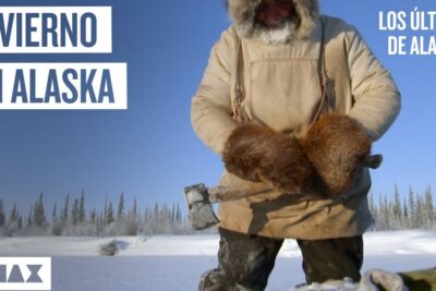 Persona con parka y manoplas de piel sosteniendo un hacha en paisaje nevado, ilustrando la alimentacion de los esquimales que comen para sobrevivir en condiciones extremas