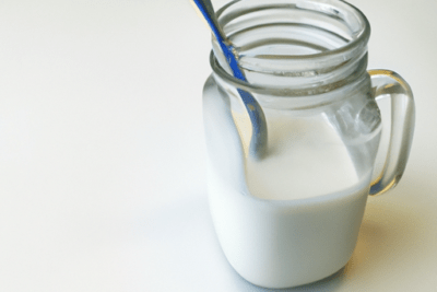 Jarra de vidrio con leche y cuchara que representa la importancia de evitar consumir leche caducada despues de 3 meses.