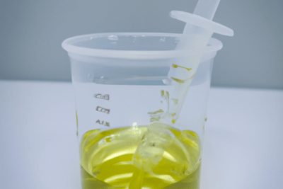 Vaso medidor y jeringa: la importancia de no utilizar amoxicilina caducada despues de 6 meses en jarabes, vaso plástico transparente con líquido amarillo y jeringa medidora insertada.