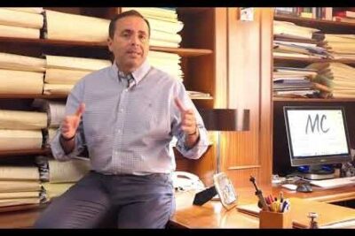 Hombre en despacho con pilas de expedientes y ordenador gestionando documentos tras legatario fallece