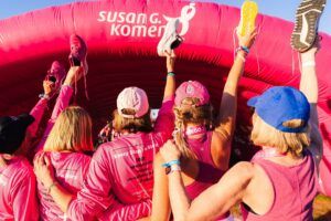 Participantes con camisetas y gorras rosas alzan zapatillas bajo un arco inflable en una caminata solidaria que logra awareness consideracion y conversion con tu publico objetivo.