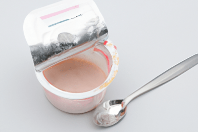 Vasito de yogur abierto con tapa parcialmente levantada y cuchara, ilustrando los peligros de consumir yogur caducado que debes saber