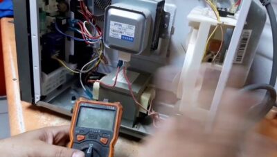 Interior abierto de microondas gira con multímetro midiendo magnetrón, transformador y cableado