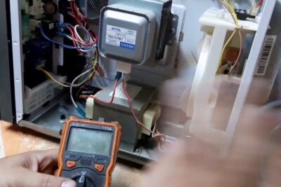 Interior abierto de microondas gira con multímetro midiendo magnetrón, transformador y cableado
