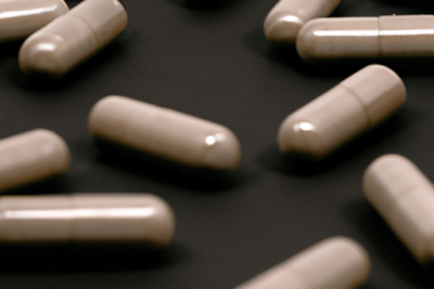 Cápsulas beige dispersas sobre fondo oscuro, advertencia sobre oxitocina caducada un peligroso riesgo para la salud.