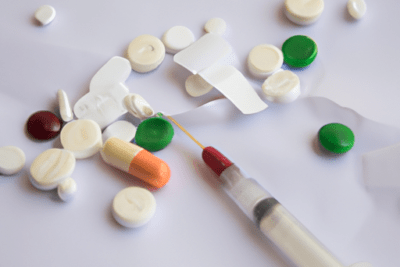 Pastillas de varios tamaños, una cápsula bicolor y una jeringa dispersas que evocan la pregunta pasa algo si un medicamento esta caducado