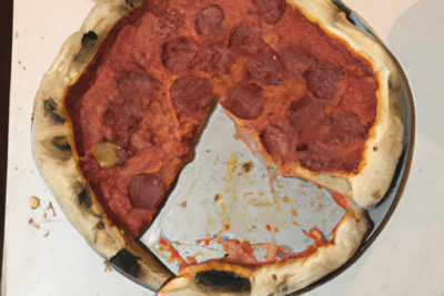 Pizza caducada 5 dias es seguro comerla o debemos evitarla, pizza de pepperoni sobre bandeja con una porción faltante y bordes parcialmente quemados