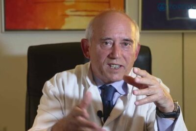 Médico de edad avanzada en bata gesticulando y explicando posibles causas de síntomas de salud.