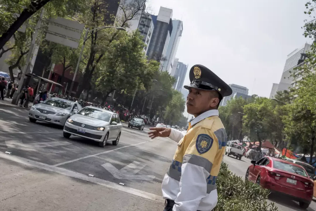 Agente de tránsito con uniforme y gorra dirigiendo vehículos en una avenida concurrida mientras surge la duda de que consecuencias hay si insultas a un policia de transito.
