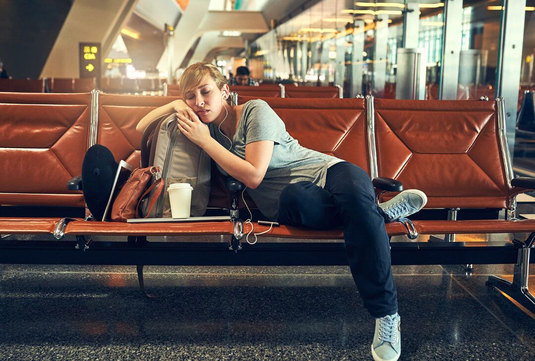 Mujer dormida en un banco del aeropuerto apoyada en su mochila, ejemplo de que es el jet lag y como afecta a una persona.