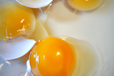 Huevos crudos abiertos y yemas a la vista: que hacer con los huevos caducados despues de 4 dias - ideas y usos, yemas brillantes sobre un plato blanco con cáscaras partidas.