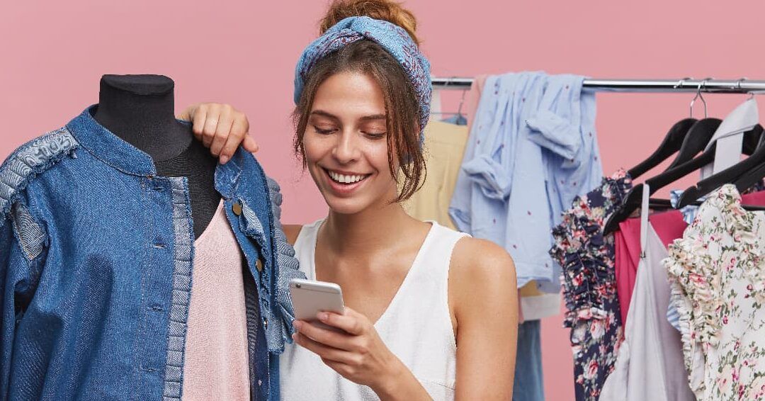 Compradora sonriente revisando su móvil entre prendas, buscando qué hacer si el vendedor de vinted no envia tu paquete.