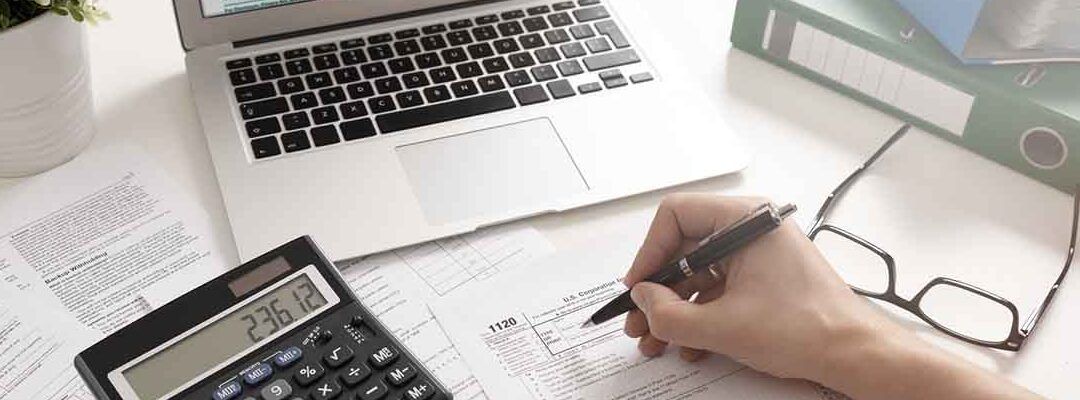 Mano rellenando formularios fiscales junto a calculadora y portátil, que hacer si la declaracion del irpf sale negativa descubre aqui.