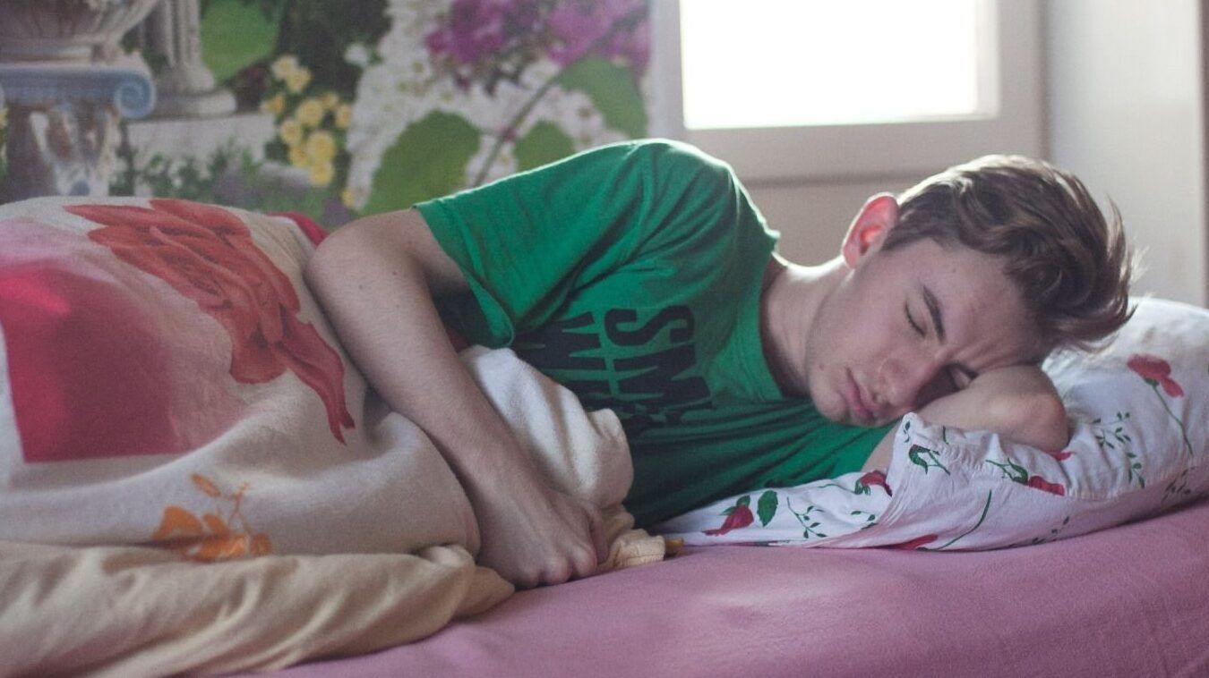 Joven acostado de lado durmiendo en una cama con almohada y cobija floral, imagen para temas de sueño y reflexiones como que ocurre al preguntar la hora en un sueno lucido descubre la respuesta aqui