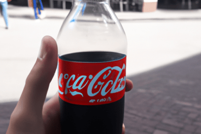 Mano sosteniendo una botella de refresco en la calle, que pasa si bebo una coca cola zero caducada