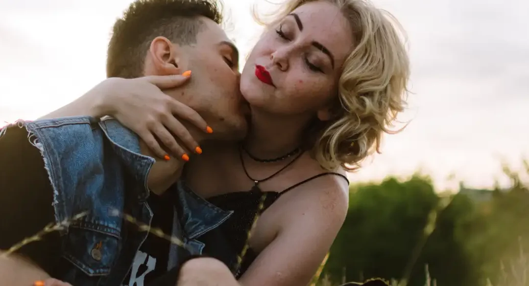Pareja abrazada en un prado al atardecer mientras él besa su cuello, que pasa si beso el cuello de mi novio descubre las respuestas aqui