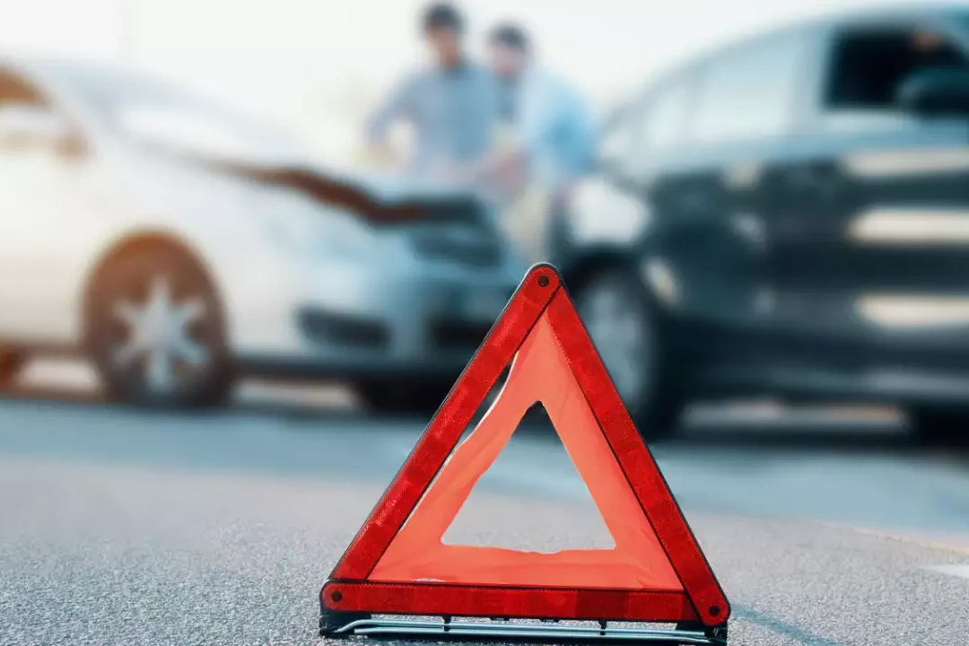 Triángulo de emergencia en primer plano frente a coches chocados que muestra que pasa si el otro conductor no tiene seguro y me choca