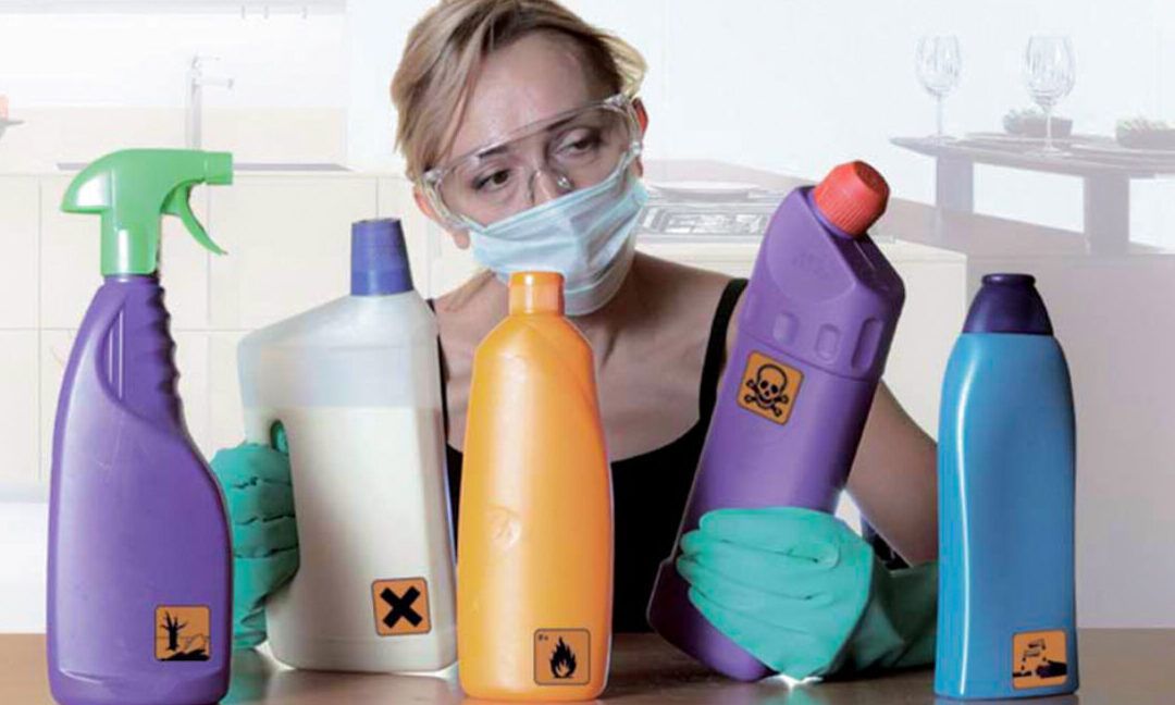 Persona con guantes, mascarilla y gafas examinando varias botellas de limpieza que ilustra que pasa si juntas lejia y amoniaco descubre la peligrosa reaccion quimica.