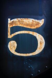 Placa metálica envejecida con el número 5 visible, que representa el numero descubre su significado y simbolismo