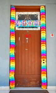 Puerta de madera adornada con guirnaldas multicolor y cartel 'Party Time', que representa el numero significado aqui