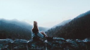 Persona sentada en un muro rocoso mirando un valle montañoso brumoso que representa emoji descubre significado curiosidades