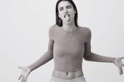 Mujer joven con expresión juguetona sacando la lengua y extendiendo los brazos, que significa hola en espanol descubrelo aqui