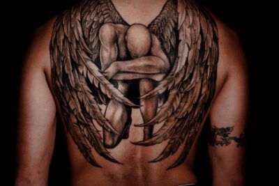 Tatuaje en la espalda de alas realistas que envuelven una figura humana; que significa tatuaje nube en clave simbólica
