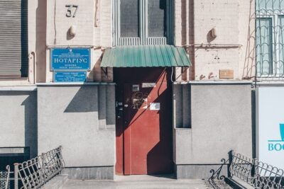 Puerta roja en una fachada con marquesina verde y placa azul que simboliza el numero