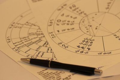 Hojas con ruedas astrológicas, glyphs zodiacales y un bolígrafo sobre la mesa que simboliza piscis astrologia en contexto de cartas natales