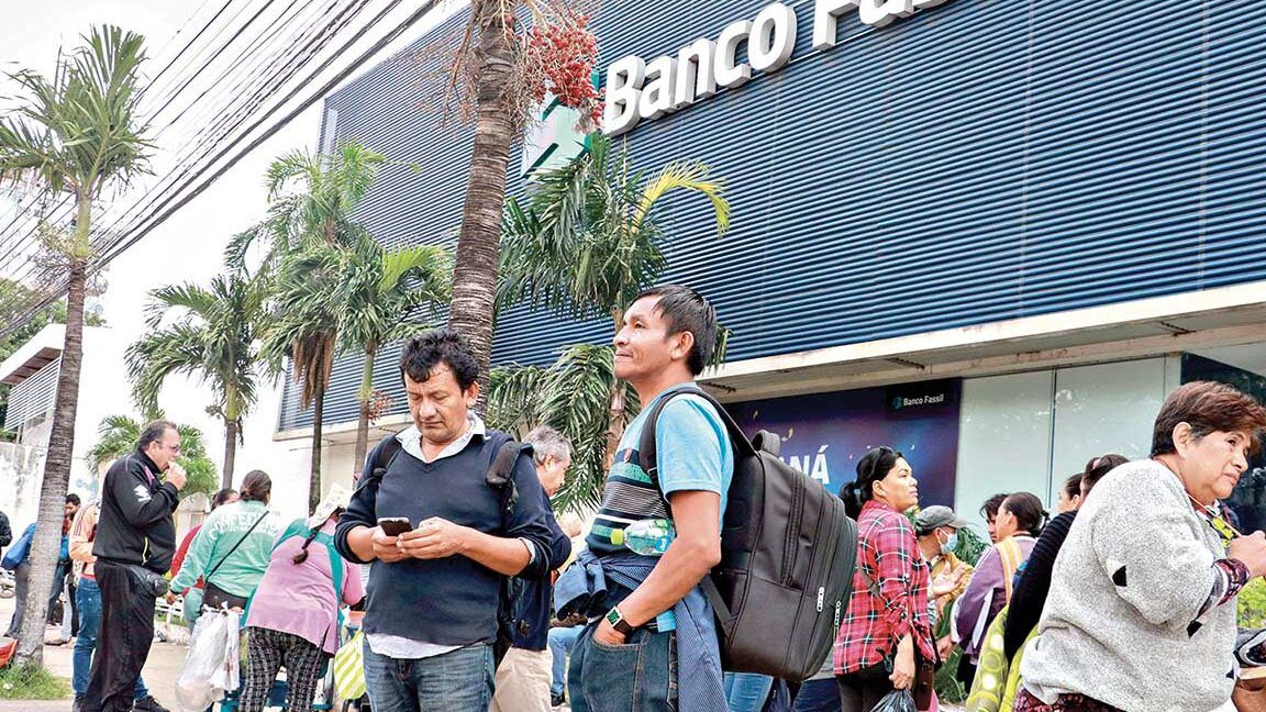 Personas haciendo fila y esperando fuera de una sucursal bancaria, situación que ilustra que sucede cuando un banco quebra en bolivia conoce las consecuencias legales y financieras
