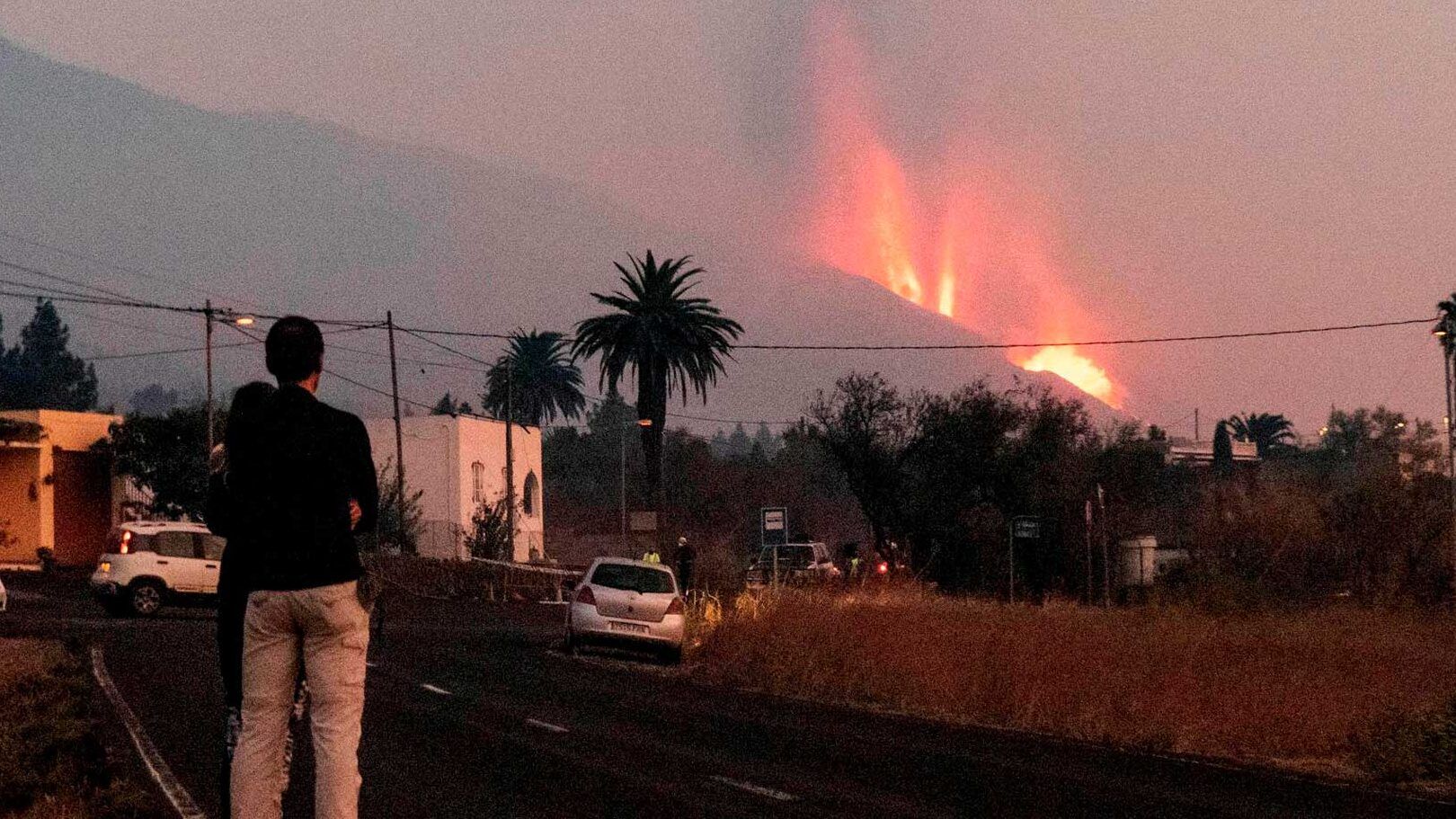 Personas observando una erupción volcánica con columnas de humo y lava cerca de una carretera, que sucede si inhalas gases toxicos descubre las consecuencias aqui