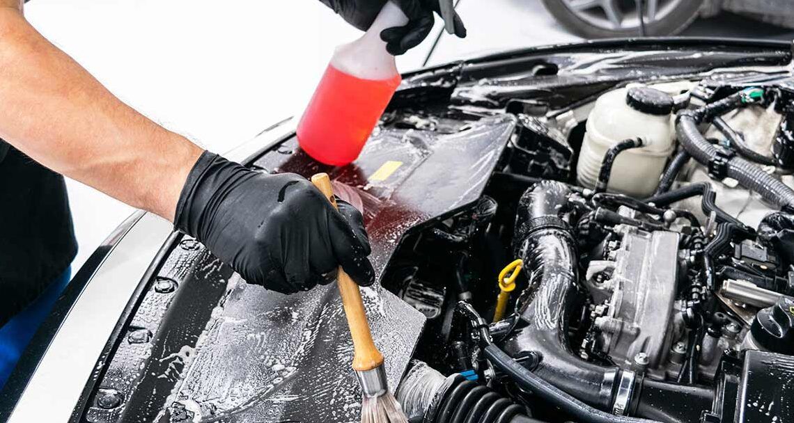Persona con guantes negros limpiando el compartimento del motor con un cepillo y un spray, que sucede si le pones gasoleo agricola a tu coche descubrelo aqui