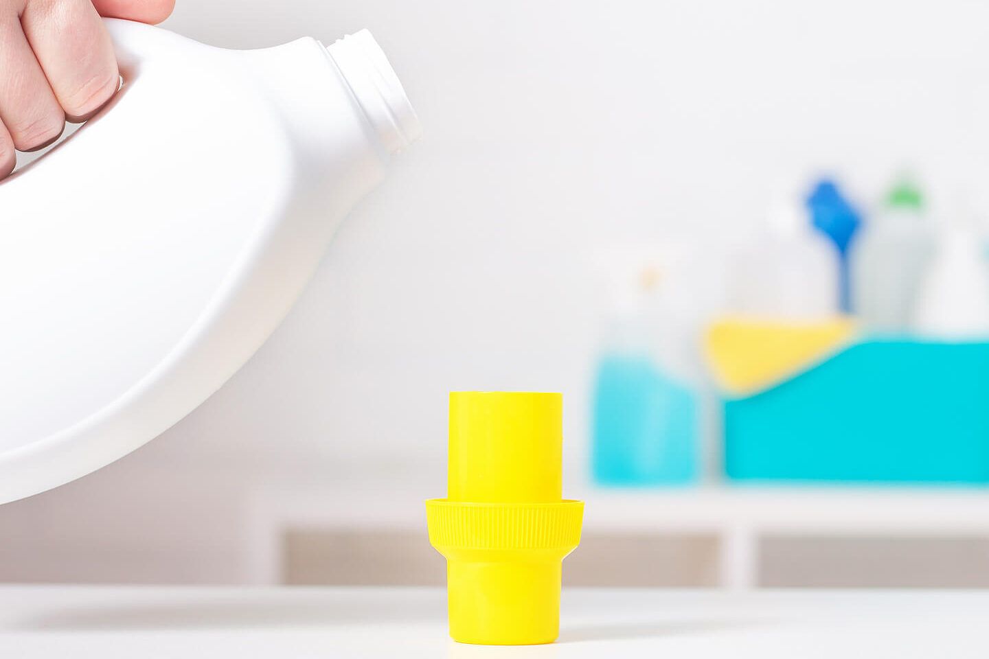 Envase blanco vertiéndose junto a un tapón amarillo y productos de limpieza difuminados en el fondo que sugiere que sucede si mezclas lejia y amoniaco descubre los peligros de esta combinacion