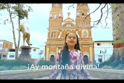 Niña frente a iglesia colorida y estatua en una plaza típica de la region antioquia.