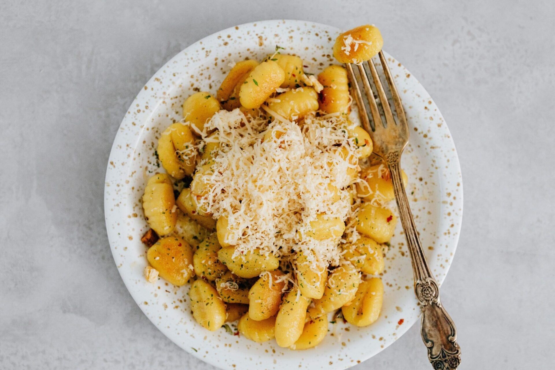 Plato de noquis dorados con queso rallado y tenedor, se pueden hacer noquis sin huevos todo lo que necesitas saber
