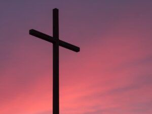 Silueta de una cruz oscura sobre un cielo rosado al atardecer que evoca significado cruz simbolo historia religion cultura.