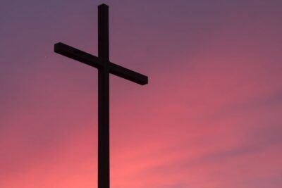 Silueta de una cruz oscura sobre un cielo rosado al atardecer que evoca significado cruz simbolo historia religion cultura.